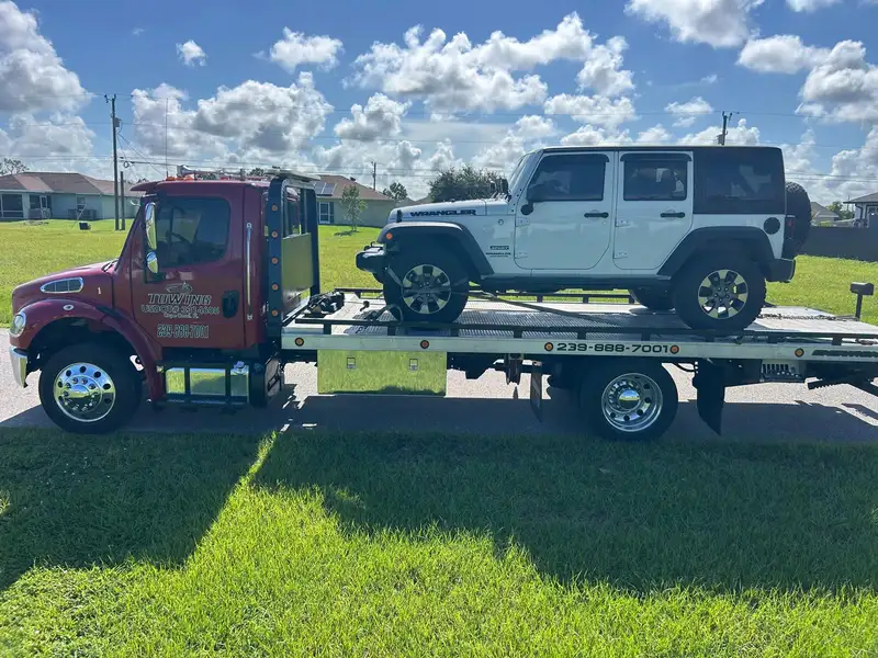 Vista de lado de la grúa roja con un Jeep Wrangler blanco en la plataforma