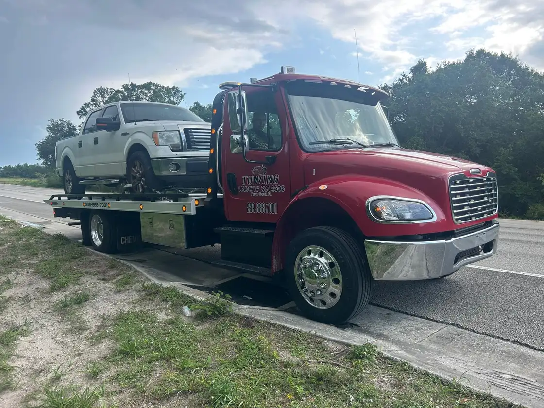 Red flatbed tow truck stopped at the side of a highway with a pickup loaded