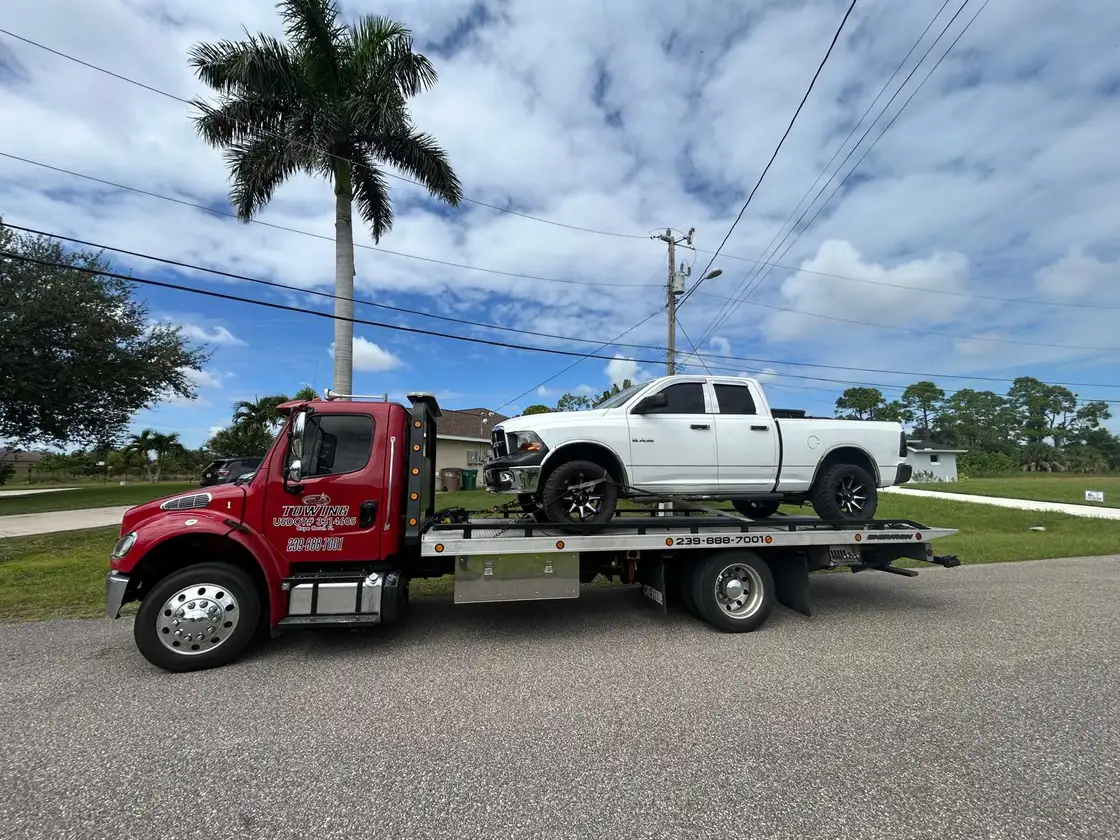 Red flatbed carrying a white pickup on a Florida street with a palm tree